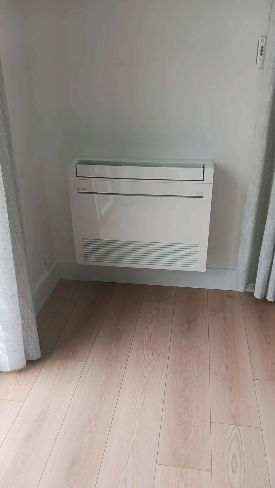 Climatiseur console Mitsubishi Electric installé au sol le long d'un mur à Melun (77)